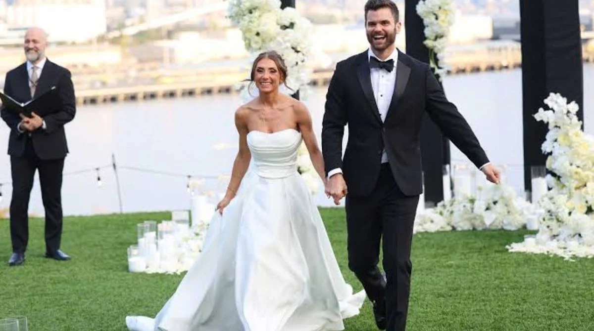 A bride laughing in her wedding gown next to her groom and a female officiant during a ceremony on Married at First Sight Season 20.