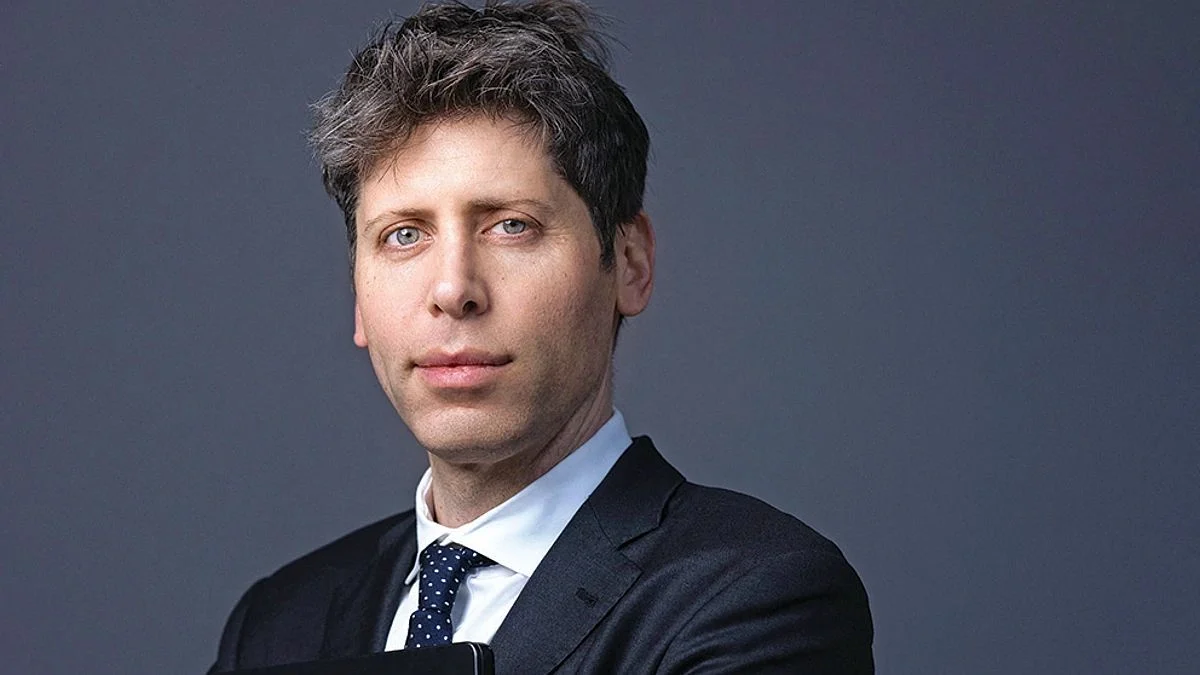 Close-up studio portrait of OpenAI CEO Sam Altman dressed in a dark gray suit and navy blue polka-dot tie, posing against a solid slate gray background.