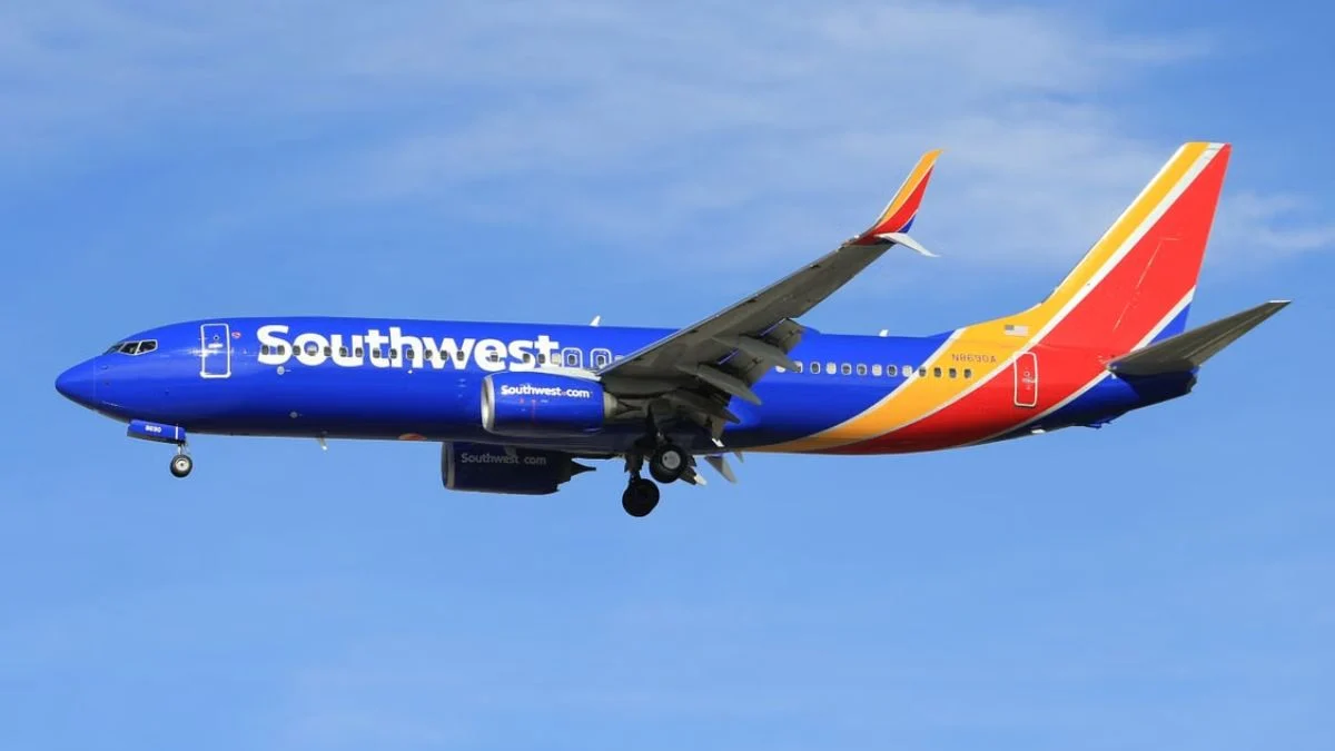 A blue, yellow, and red Southwest Airlines passenger airplane flying in a clear blue sky before landing.