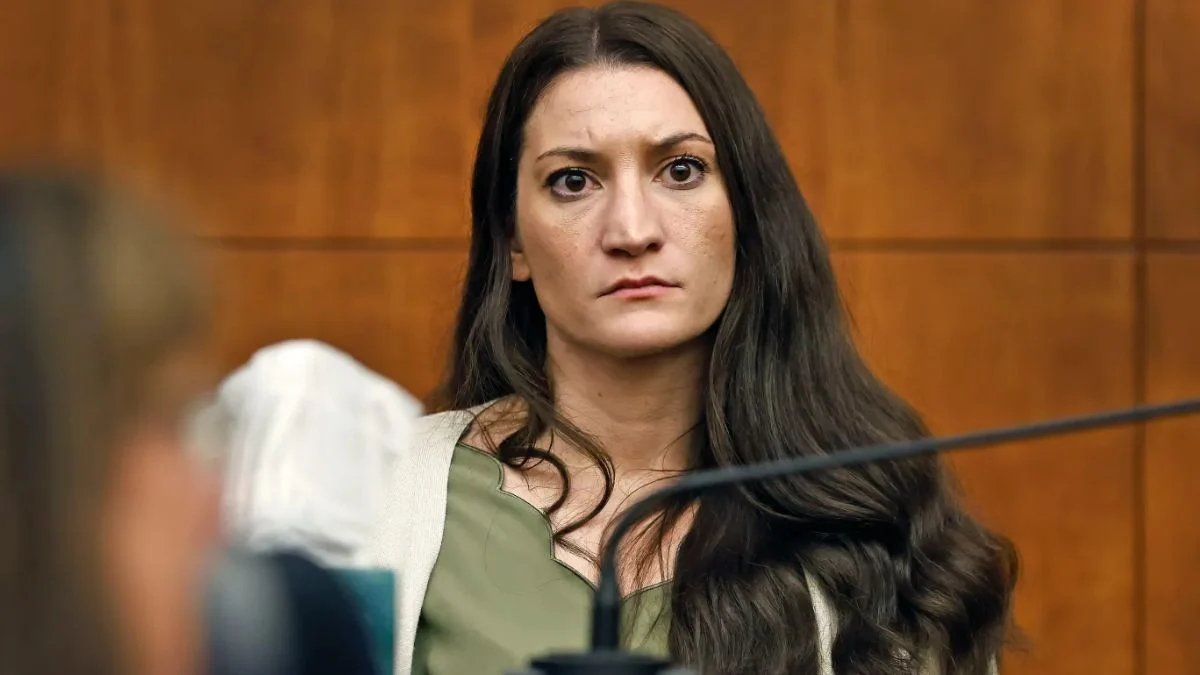 Close-up of Lindsay Clancy with long brown hair wearing a green blouse and white cardigan looking forward inside a courtroom.