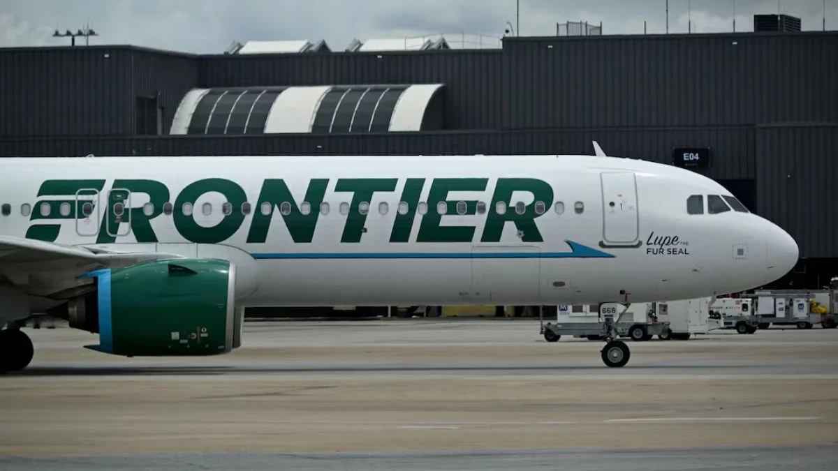 A close-up side view of a white Frontier Airlines Airbus aircraft with the green "FRONTIER" logo and "Lupe the Fur Seal" character on the tarmac.