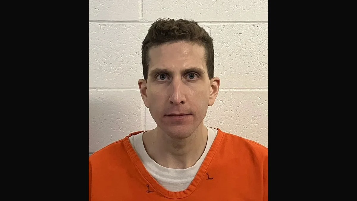 Bryan Kohberger booking mugshot in an orange prison uniform against a white brick wall.
