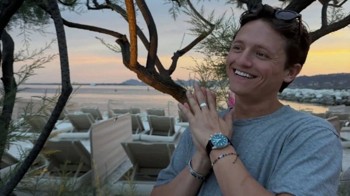 Social media personality Connor Wood smiling with hands clapped together at a beachside lounge area.