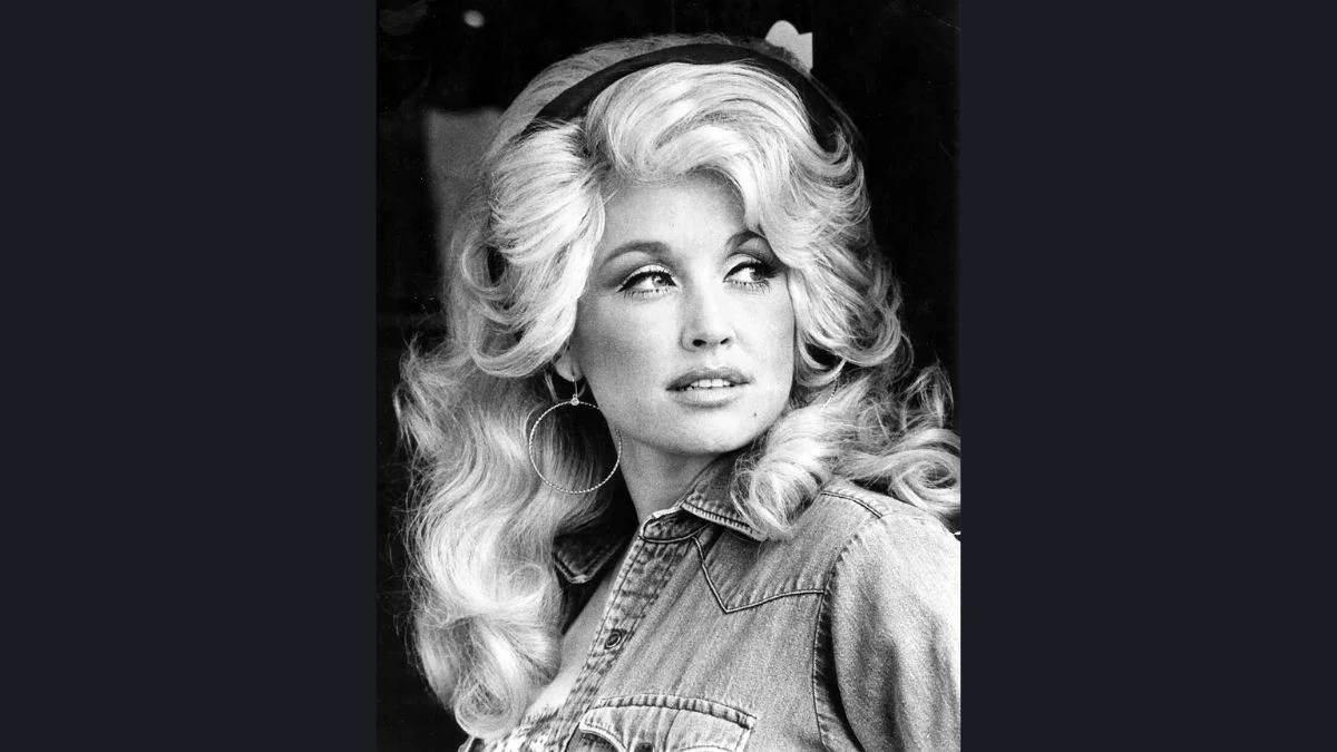 Black and white promotional portrait of a young Dolly Parton with her signature voluminous blonde hair and denim outfit