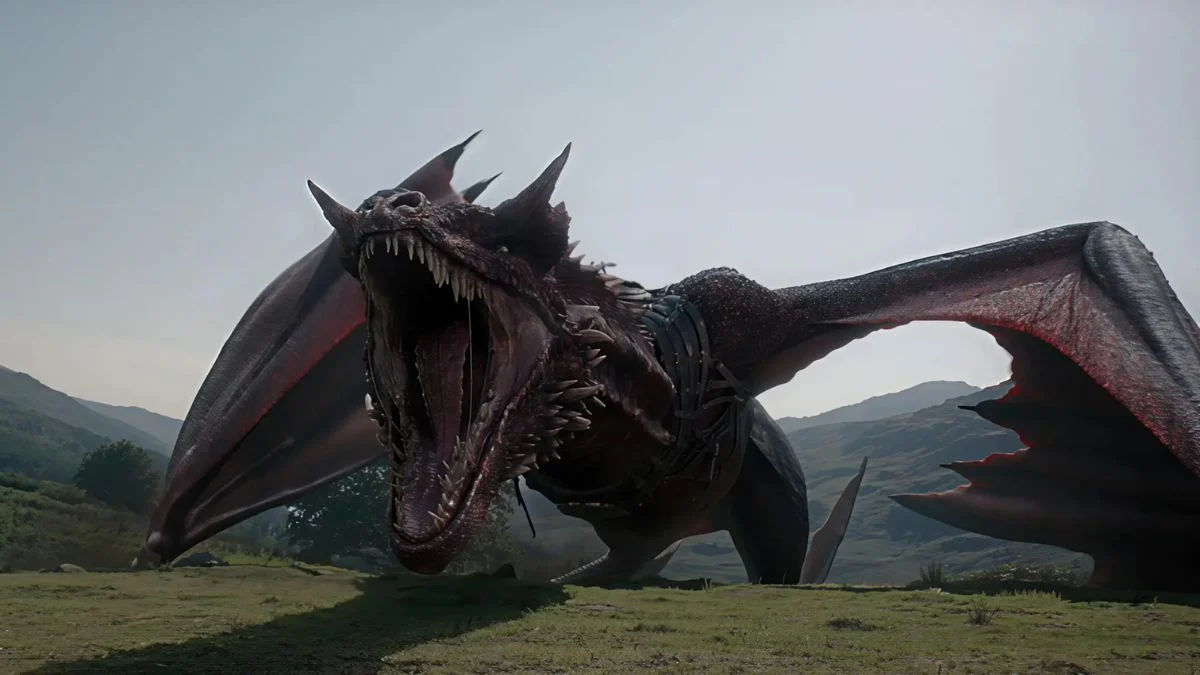 The red dragon Caraxes standing on a grassy field under a bright sky, roaring with its massive jaws wide open.