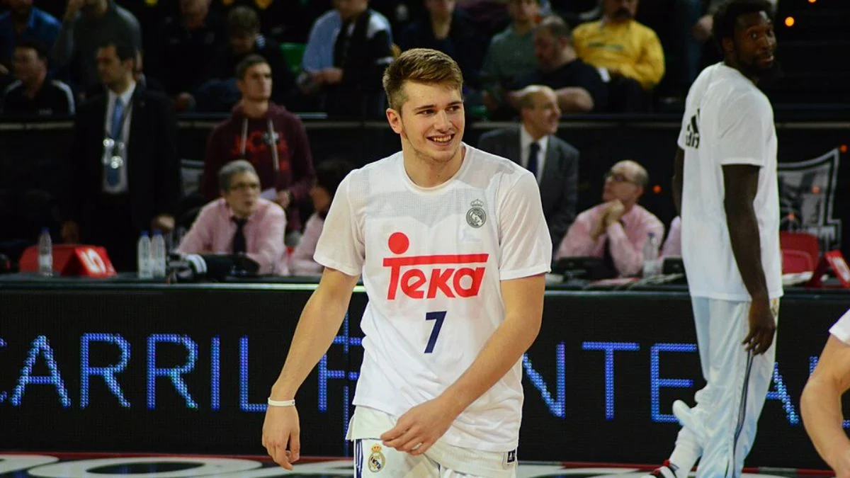Young Luka Dončić smiling on the basketball court in a white jersey with number 7.