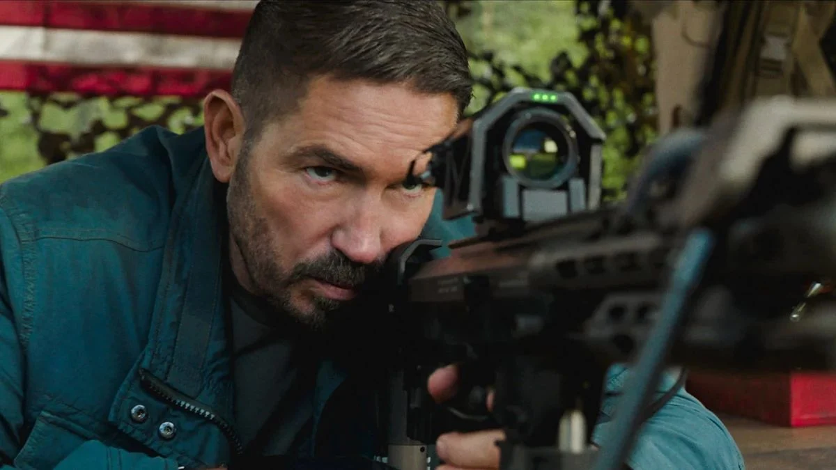 Jim Caviezel aiming a tactical rifle with an advanced optical scope in a scene from Ghost Soldier.