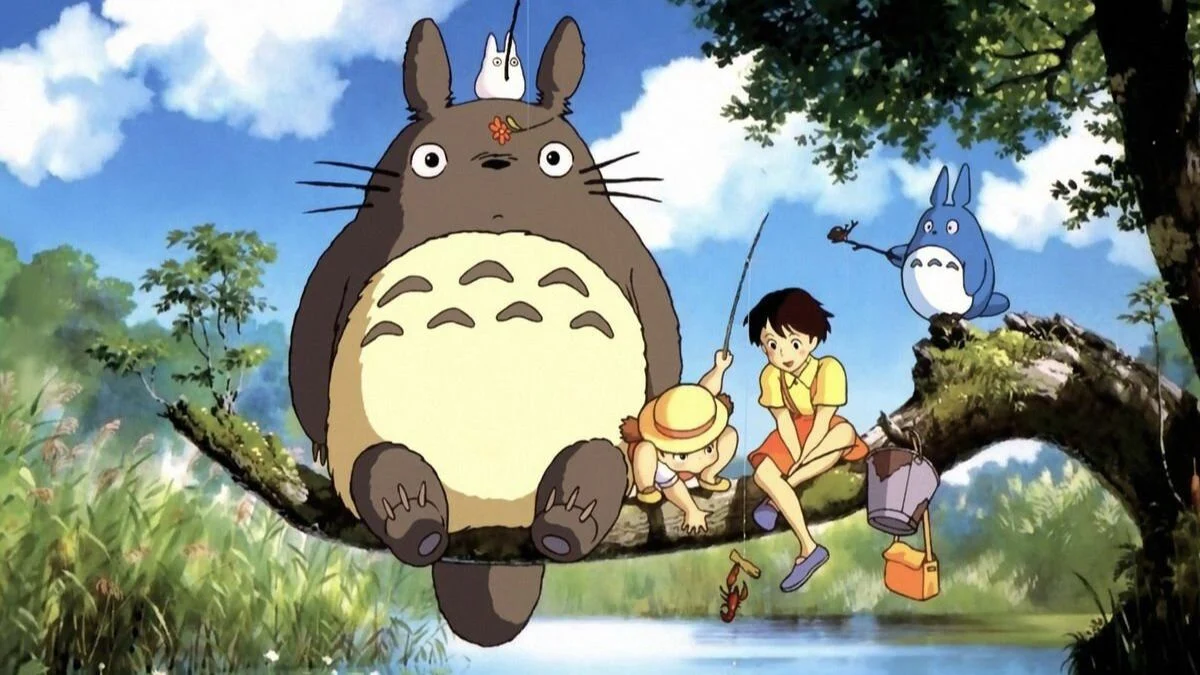 Classic illustration of Totoro sitting on a large tree branch alongside Satsuki, Mei, and smaller forest spirits.