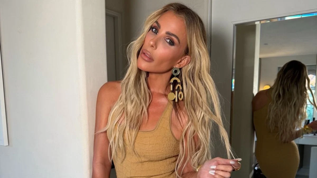Tracy Tutor posing in a tan textured top and gold statement earrings for a glam portrait.