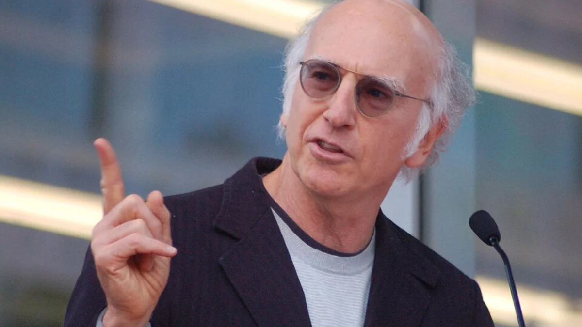 Larry David pointing his finger while speaking into a microphone.