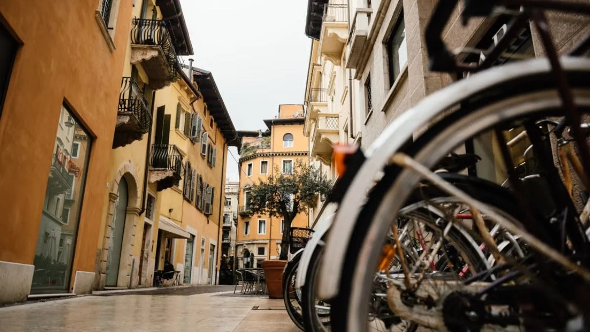 Close-up of bicycle wheels parked along a narrow, historic Italian street with colorful historic buildings in the background.