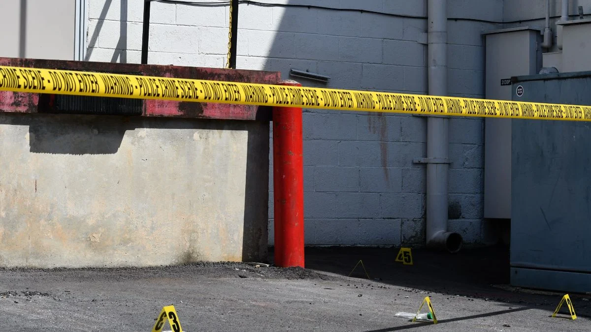 Yellow police crime scene warning tape stretched across an outdoor area with evidence markers on the ground.