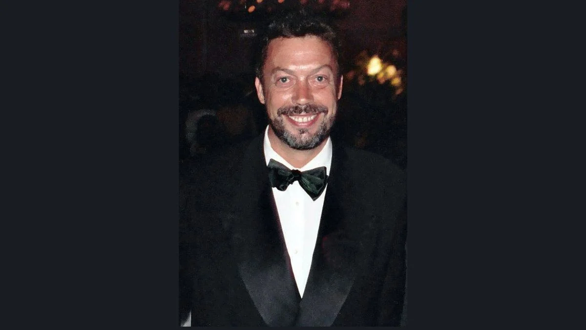 Tim Curry smiling in a black tuxedo and bowtie at a formal event.