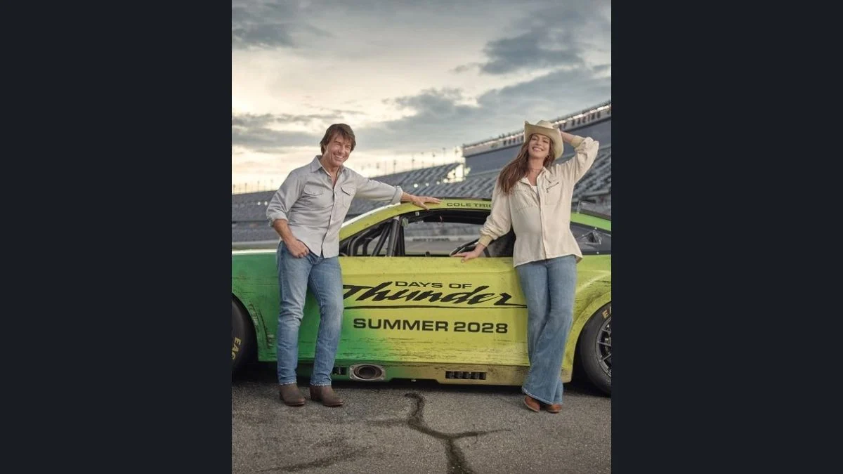Tom Cruise and Anne Hathaway standing next to a green Days of Thunder NASCAR race car
