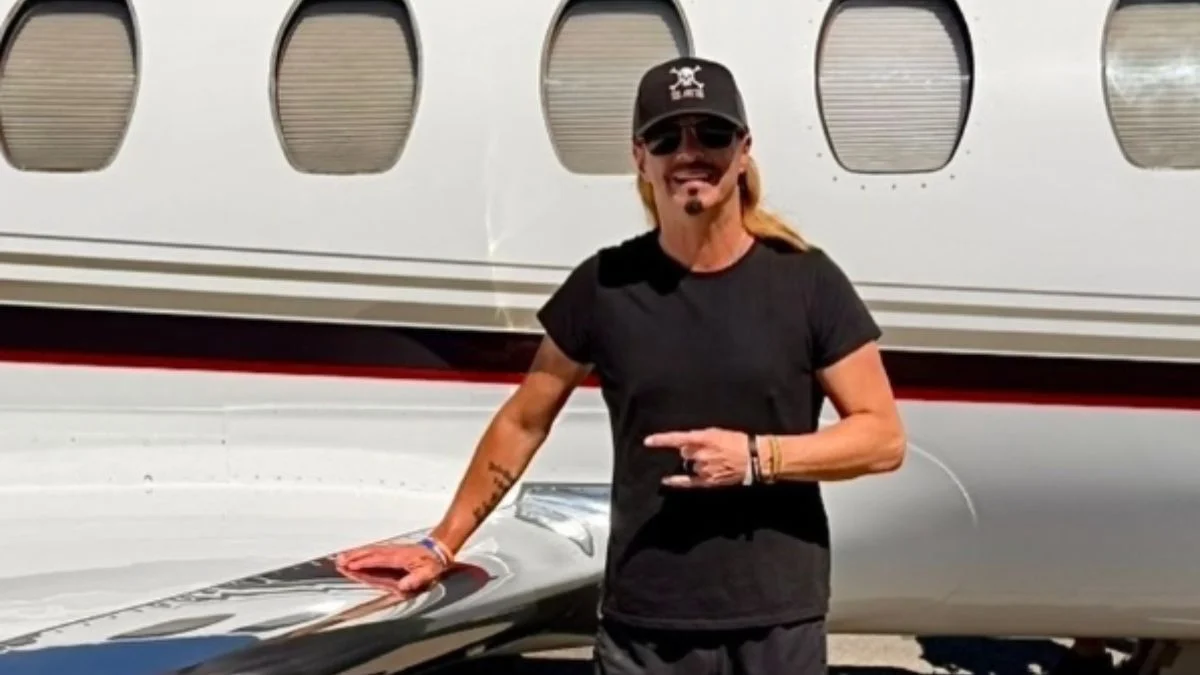 Poison frontman Bret Michaels smiling next to a private jet wearing a black cap and t-shirt