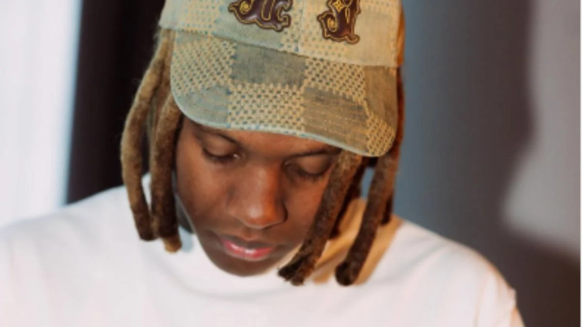 Close-up of Lil Durk wearing a plaid baseball cap and white shirt looking down during trial coverage.