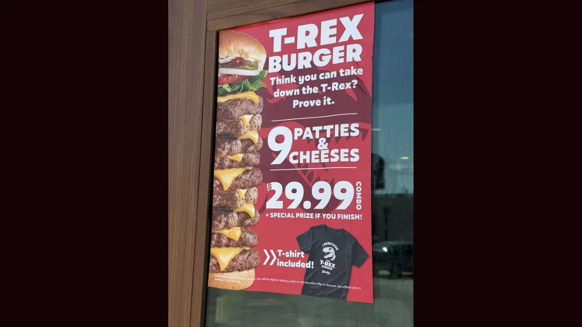 Window poster at a Wendy's restaurant advertising the T-Rex Burger challenge with 9 patties and 9 cheeses for $29.99.