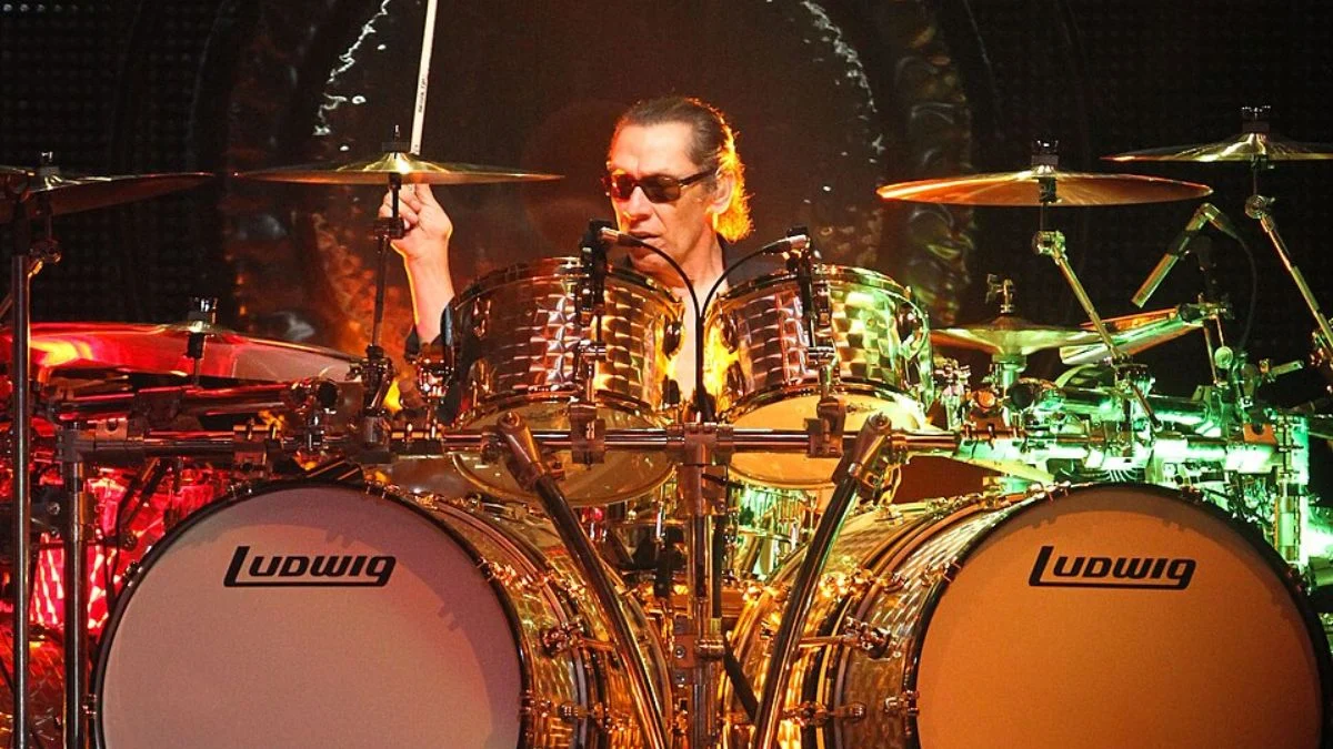 Alex Van Halen playing a massive Ludwig drum kit behind a large gong during a live concert performance.