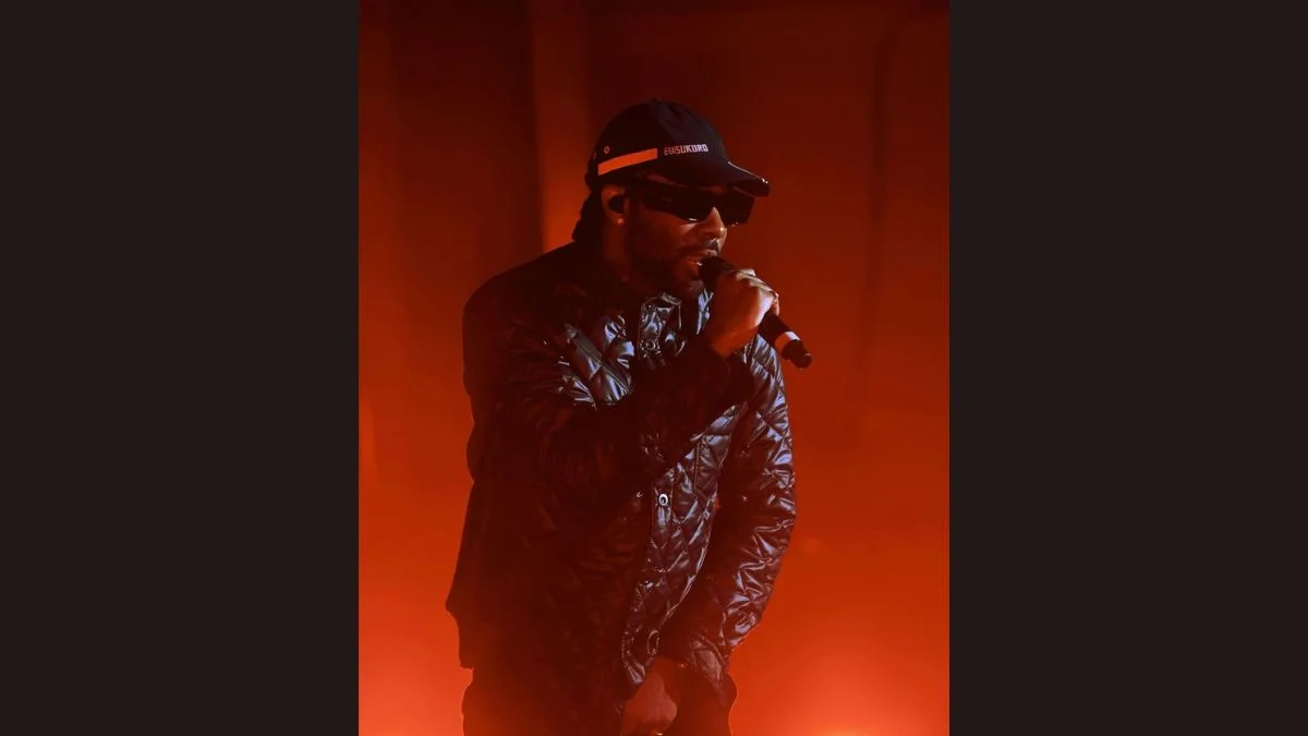 Brent Faiyaz performing live on stage with a microphone under warm stage lights.