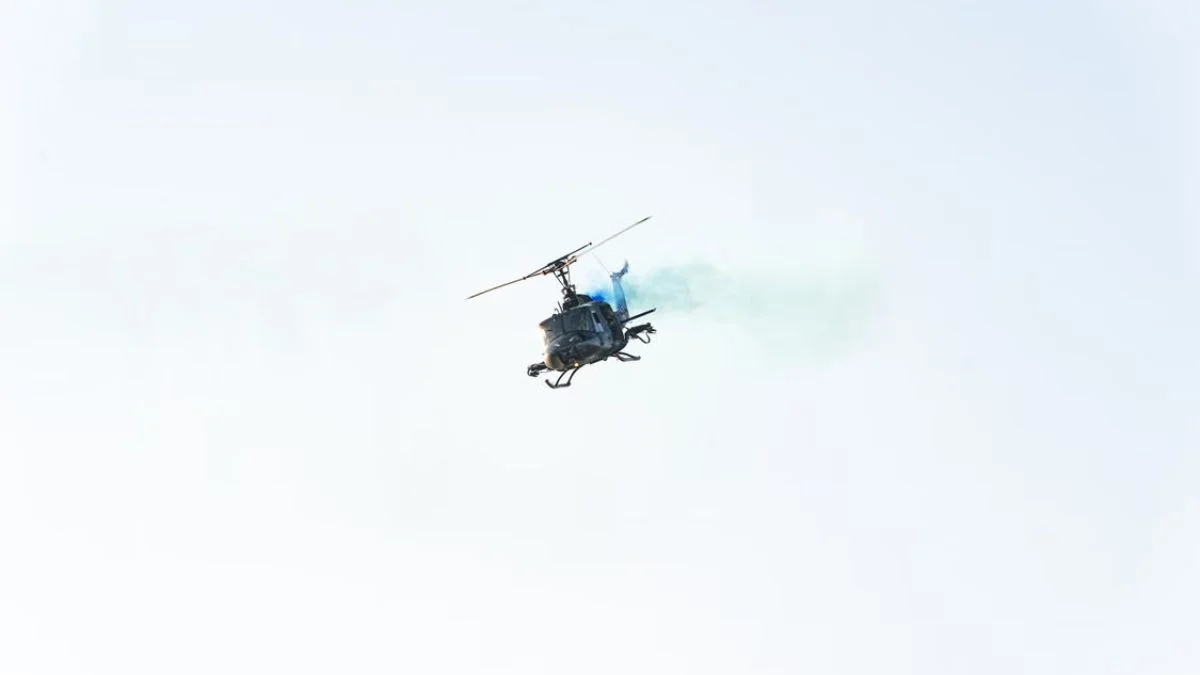 A single helicopter flying low against a bright clear sky emitting light smoke during flight.