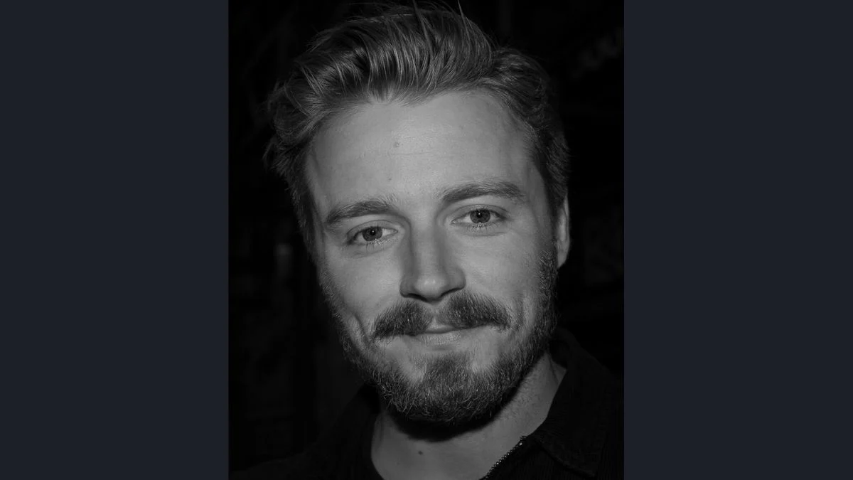 Black and white headshot of actor Jack Lowden smiling with a beard and styled hair.