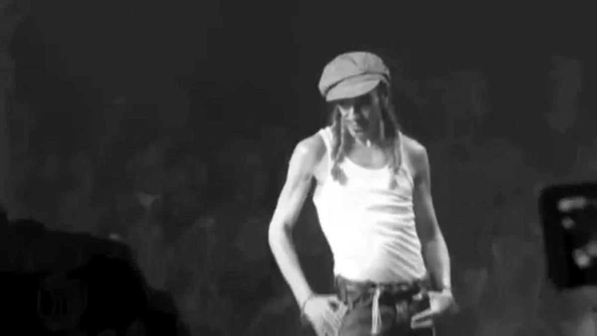 Black and white photo of fashion designer John Galliano walking the runway in a white tank top and cap.