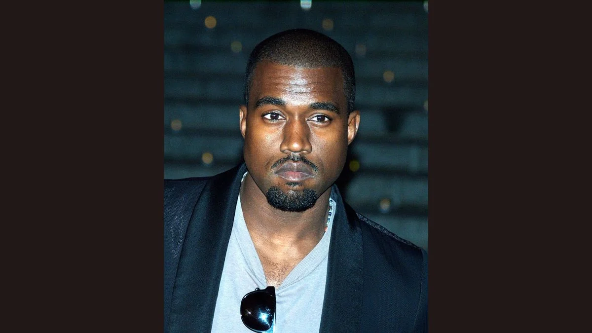 Kanye West posing at an event in a dark jacket and grey shirt, attending the Dr. Donda West Way street dedication in Chicago.