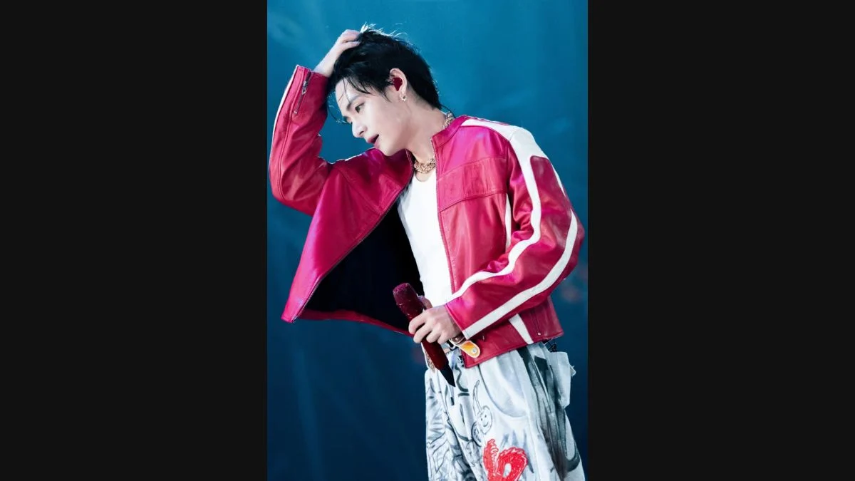 BTS member V running his hand through his hair while wearing a red jacket on stage during a concert