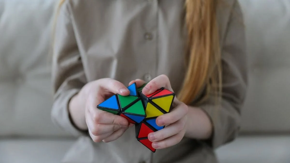 Close-up view of a person solving a colorful twisty puzzle using both hands.