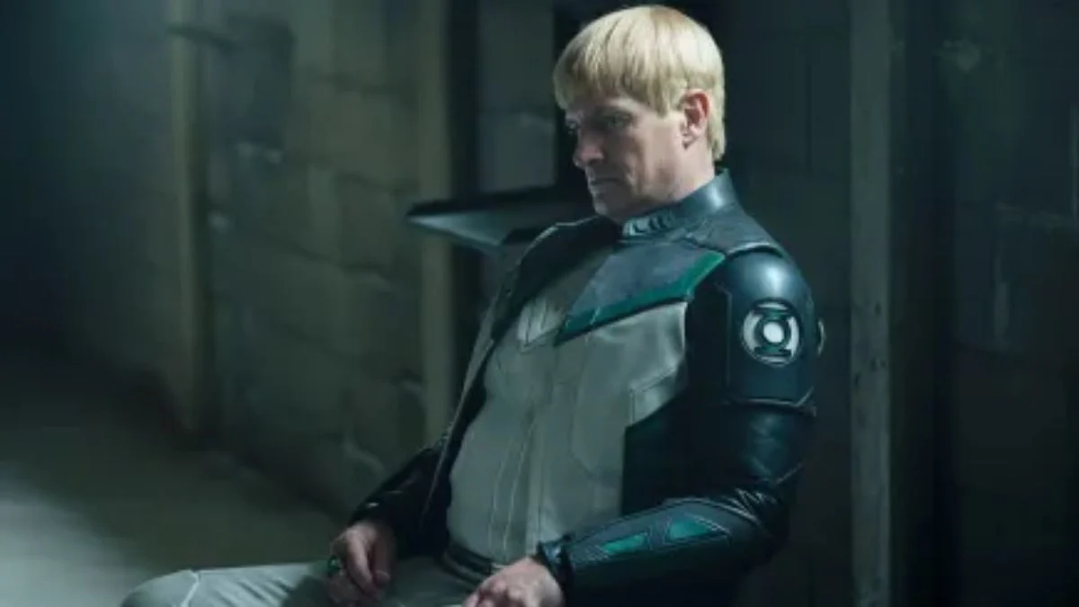 Nathan Fillion with a bowl cut wearing his Guy Gardner Green Lantern suit in a dimly lit room