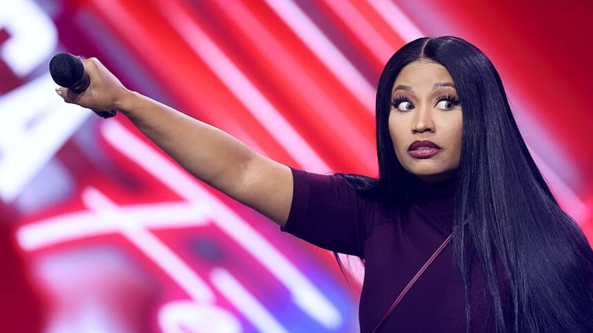 Hip-hop artist Nicki Minaj wearing a dark top, holding a microphone, and gesturing on stage