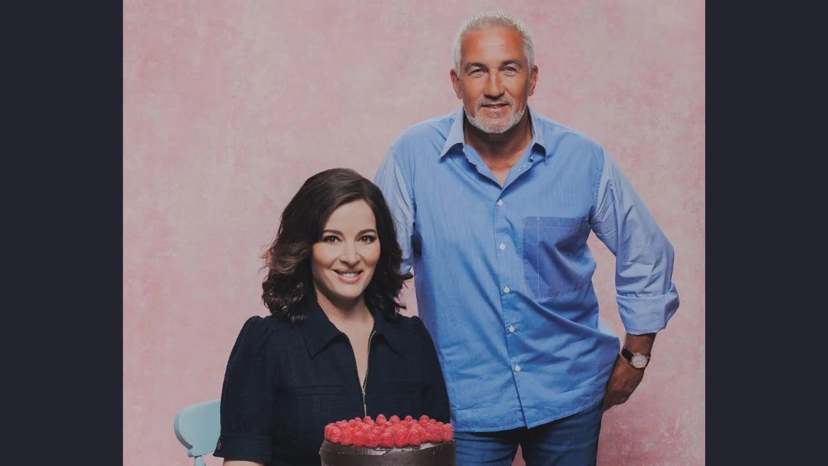 Nigella Lawson and Paul Hollywood posing together behind a chocolate raspberry cake as judges for Great British Bake Off.