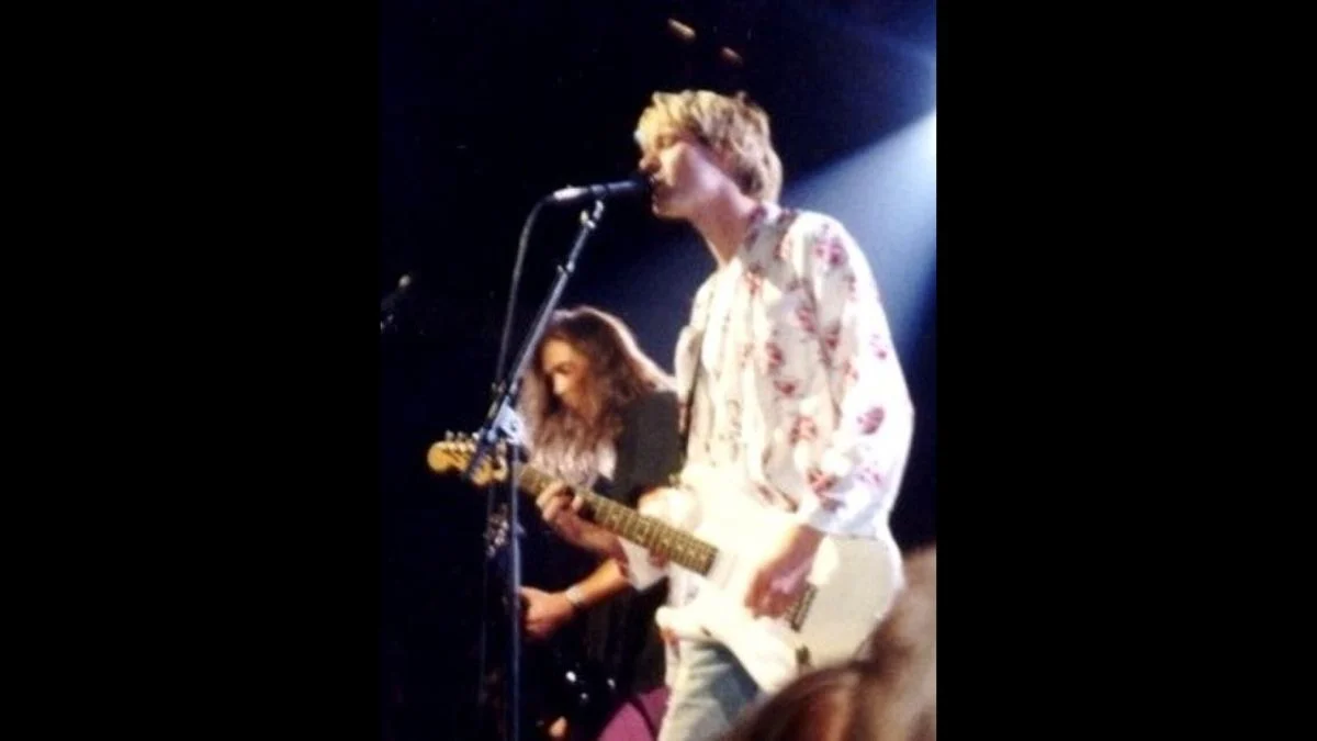 Kurt Cobain singing and playing white electric guitar live on stage with Krist Novoselic playing bass in Nirvana.