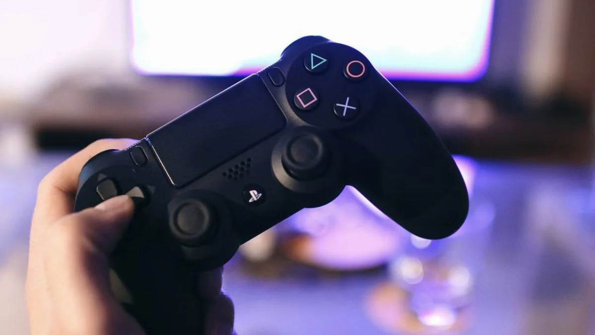 Gamer holding a dark DualShock 4 wireless controller with a lit light bar