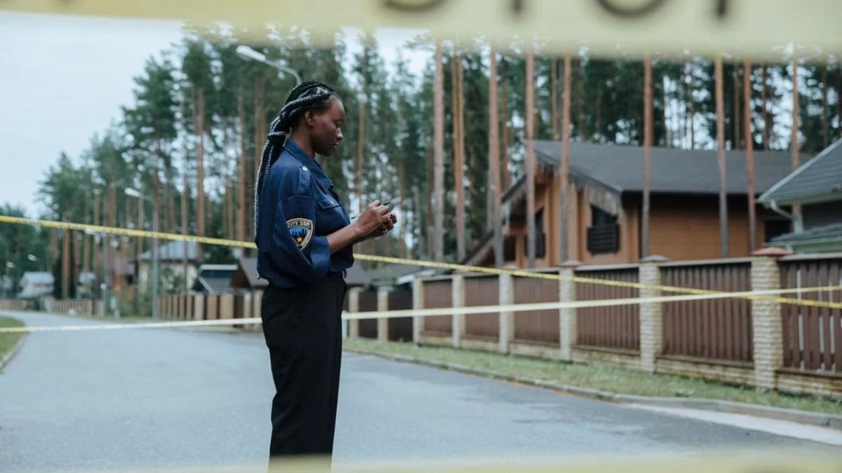 A female police officer taking notes behind yellow crime scene tape in a residential area