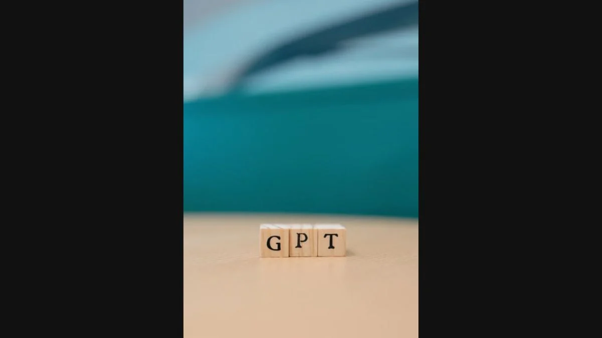 Small wooden letter blocks spelling out GPT on a neutral surface with a teal background