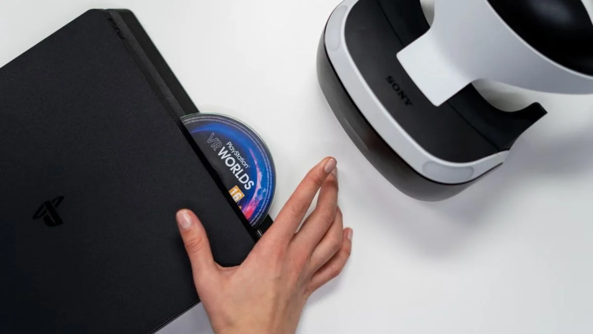 A hand inserting a PlayStation 4 game disc into a console next to a PS VR headset.