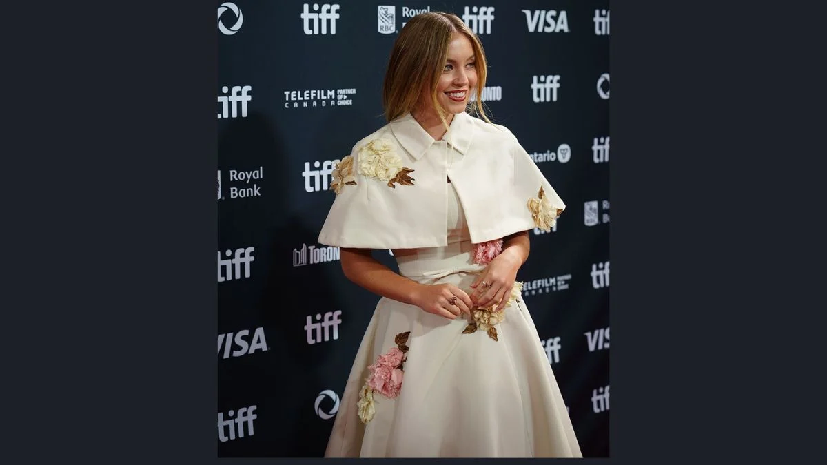 Sydney Sweeney smiling on the red carpet in a white cape dress at the Toronto International Film Festival.