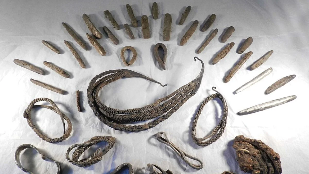 Dozens of Viking Age silver ingots, braided arm rings, and metal fragments arranged on a white backdrop.