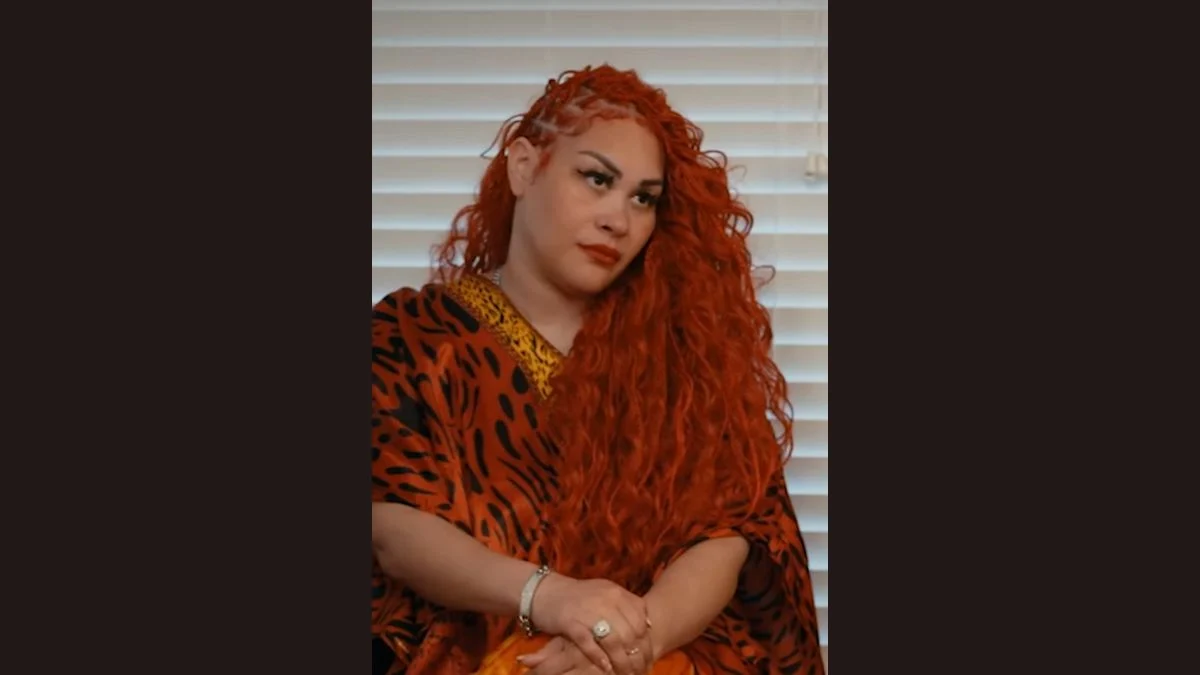 R&B singer Keke Wyatt wearing an orange patterned outfit and red curly hair looking to the side.