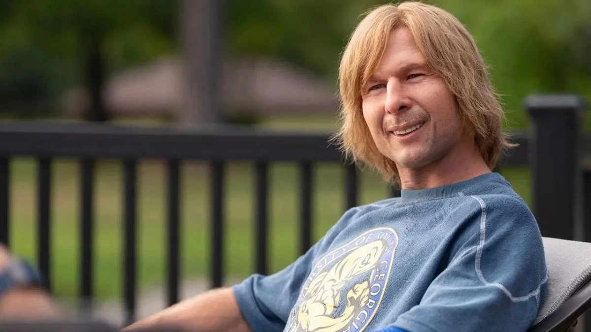 Glen Powell disguised in blonde hair prosthetics as Chad Powers sitting outdoors