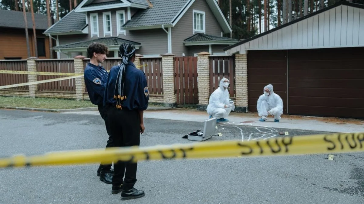 Law enforcement officers and forensic investigators in protective white suits inspecting evidence at a cordoned-off crime scene.