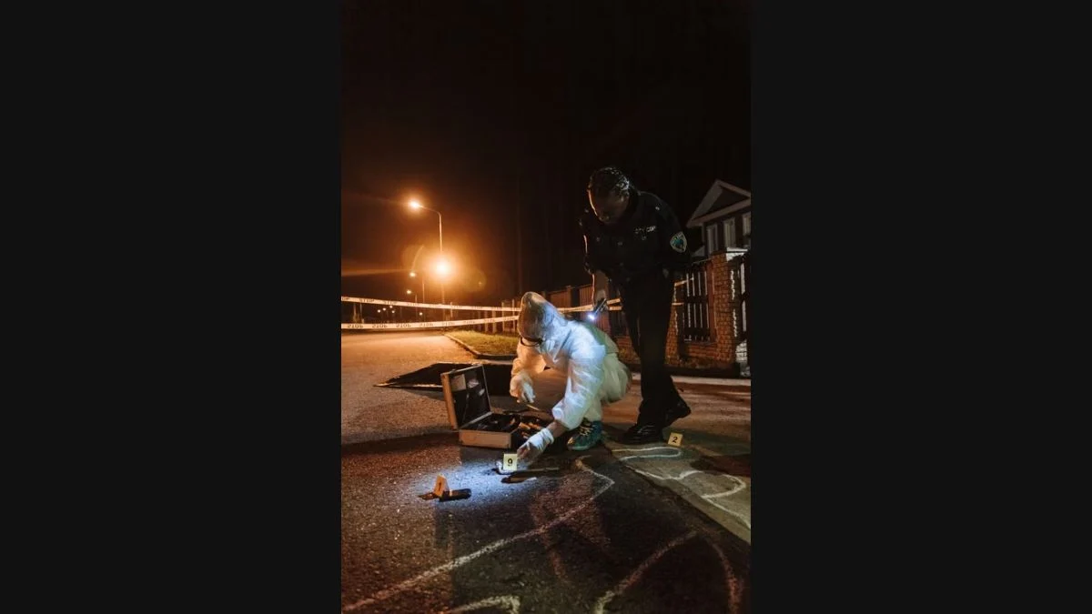 Forensic investigators examining evidence markers on a street at night with police tape in the background