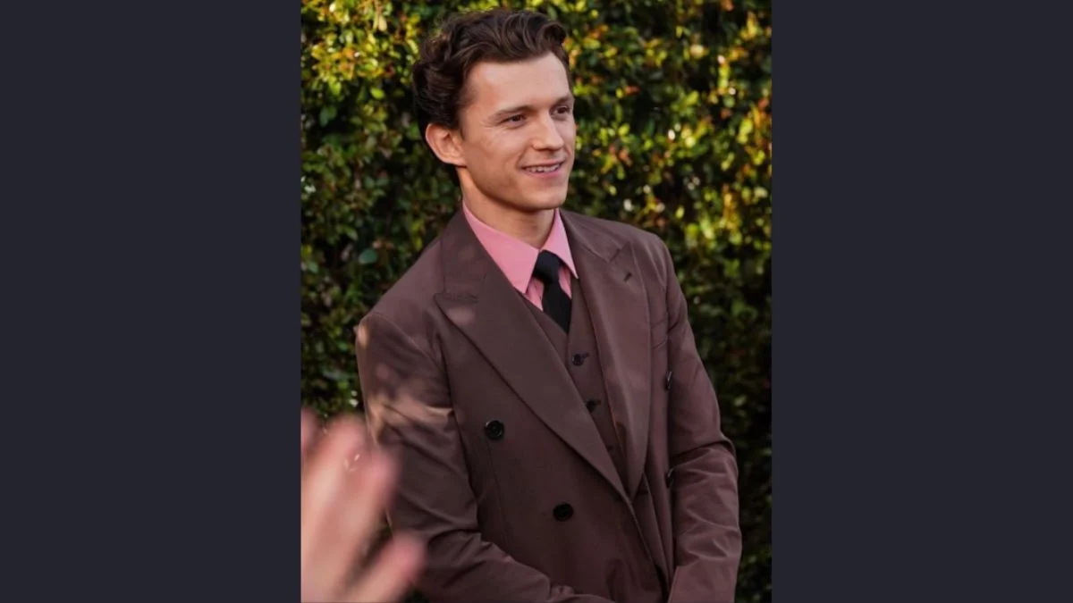 Tom Holland wearing a brown double-breasted suit and pink shirt, smiling outdoors.