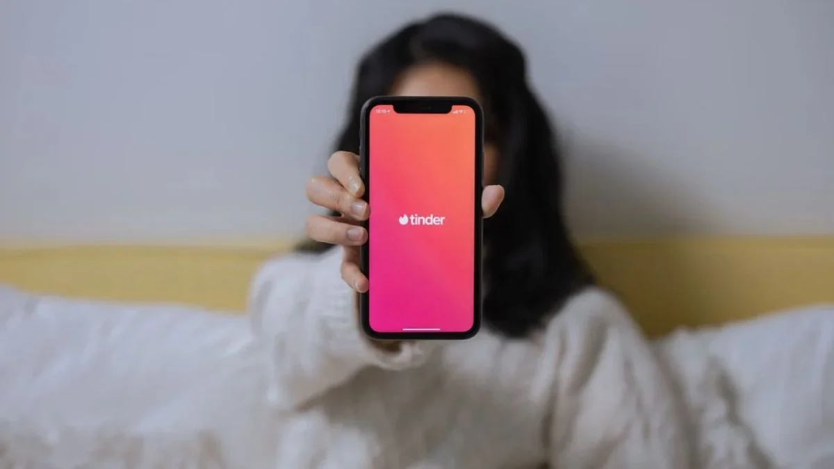 Person holding up a smartphone showing the pink and orange Tinder logo on screen
