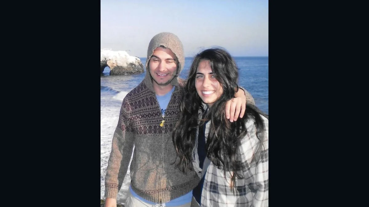 Ethan Klein and Hila Klein standing together outdoors on a beach with the ocean in the background, smiling