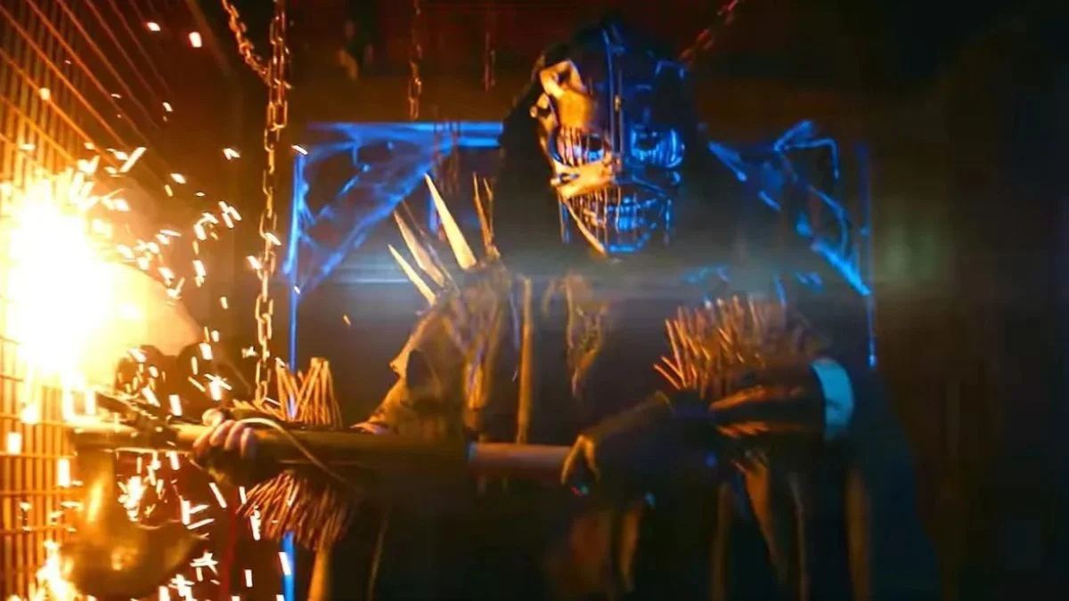 Masked figure holding a weapon in a dark haunted house attraction with sparks and chains in A24's Slayground