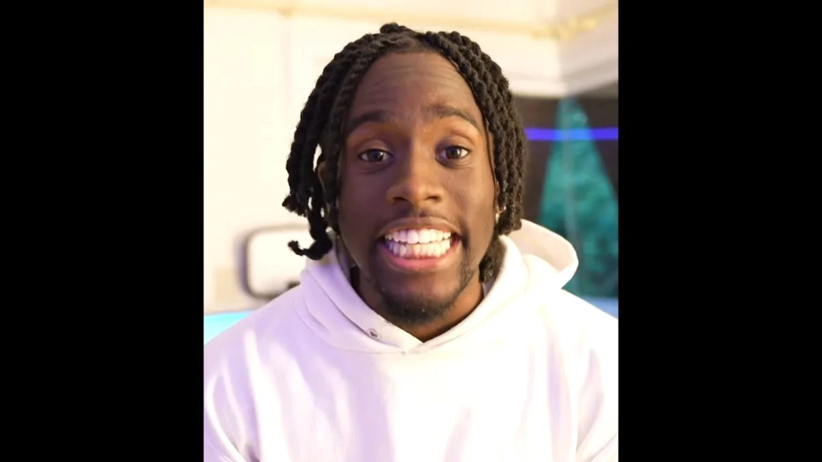 Kai Cenat wearing a white hoodie and smiling in a close-up portrait