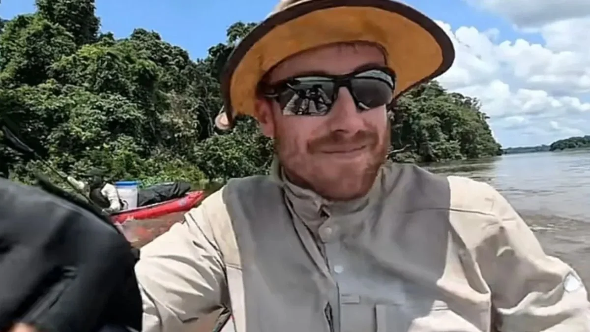 Explorer Ash Dykes smiling in a wide-brim hat, sunglasses, and high-collar expedition shirt while kayaking on the Sangha River