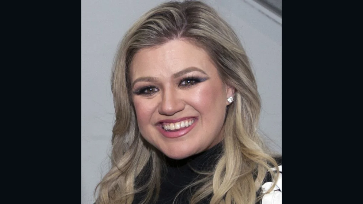 Portrait of singer and talk show host Kelly Clarkson smiling while wearing a black top.
